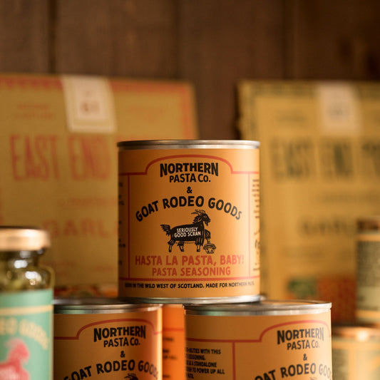 Cans of Northern Pasta Co. goat and rodeo goods with cardboard boxes in the background.