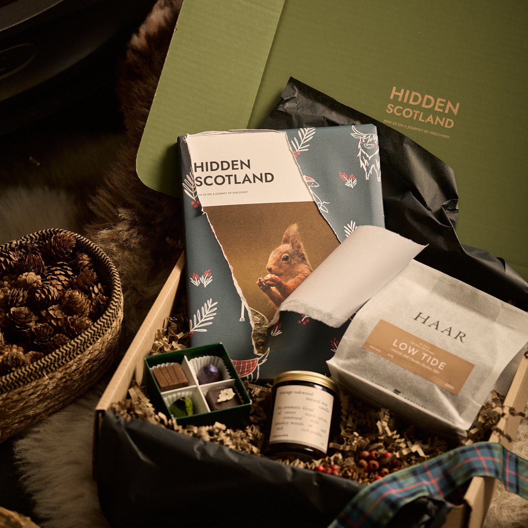 Gift box with 'Hidden Scotland' branding and various items including a jar and a book, set against a natural background.