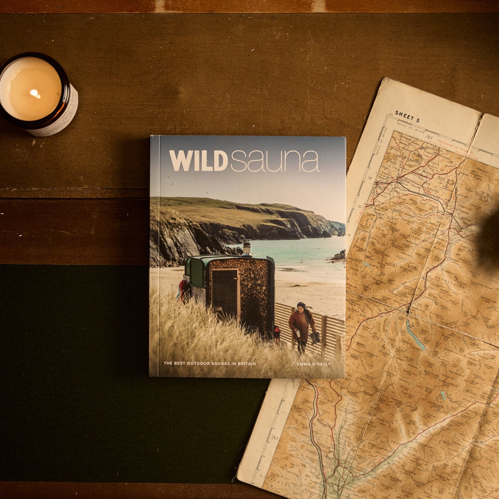 Book titled 'Wild Sauna' on a wooden surface with a candle and map.