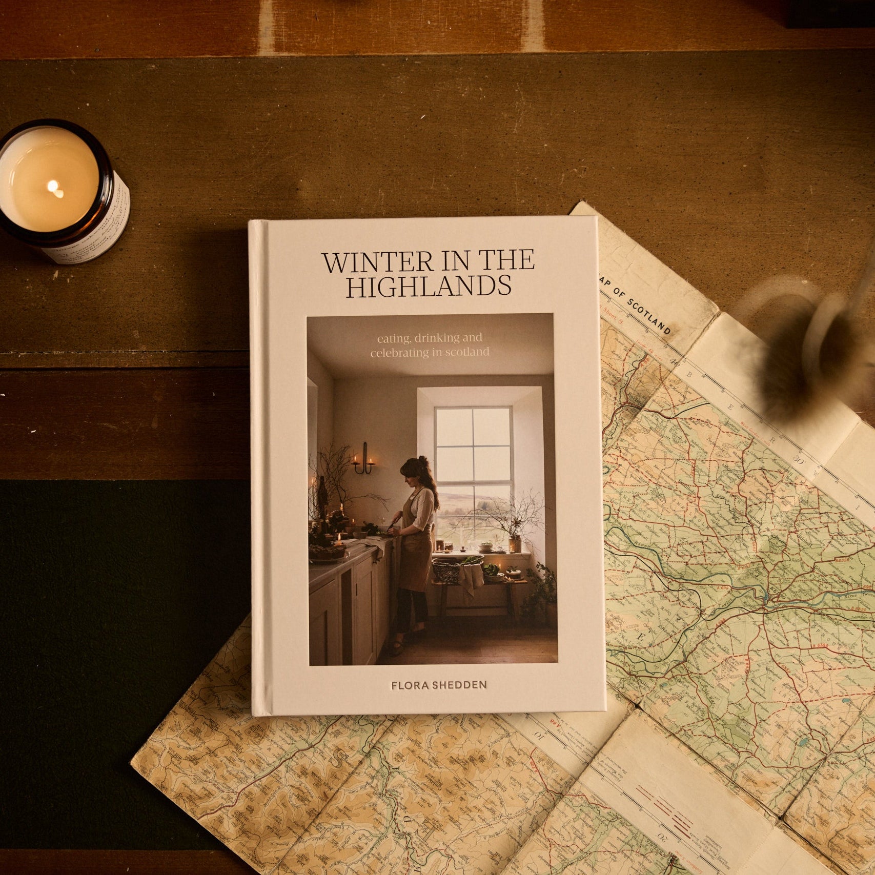 Book titled 'Winter in the Highlands' on a wooden surface with a map and candle.